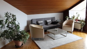 Un salon moderne comprenant un canapé, deux fauteuils, une table basse et une grande plante en pot.