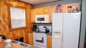 A kitchen with wooden cabinets, a microwave, an oven, a refrigerator, and a window with blinds. - Morehead Cabin on the lake (Morehead)