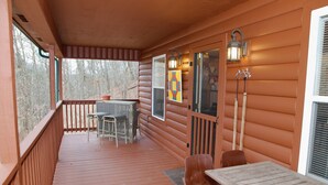 A wooden deck with a table and chairs, a window with a view of trees, and wall-mounted lights. - Morehead Cabin on the lake (Morehead)
