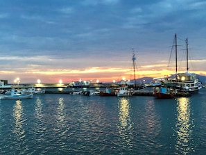 A marina with boats docked, calm water, and a sunset in the background.