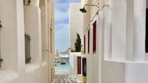 Une ruelle étroite pavée, bordée de bâtiments blancs aux accents rouges, qui mène à un port où sont amarrés des bateaux.