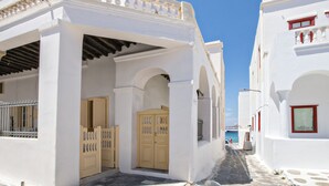 Une rue étroite bordée d’immeubles blancs, avec une porte en bois et une vue sur la mer.