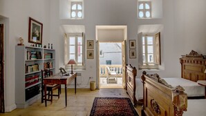 Une pièce avec un bureau en bois, des étagères à livres, un lit et une vue sur un balcon, accessible par une porte ouverte.