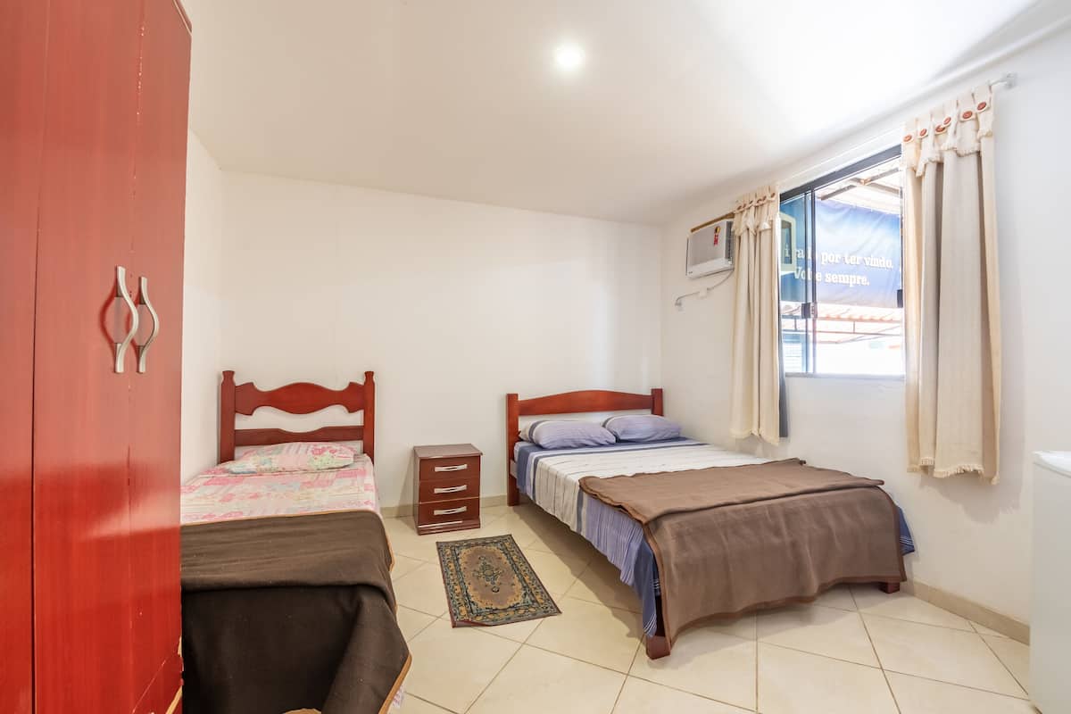 A bedroom with two beds, a wardrobe, a bedside table, and a window with curtains.