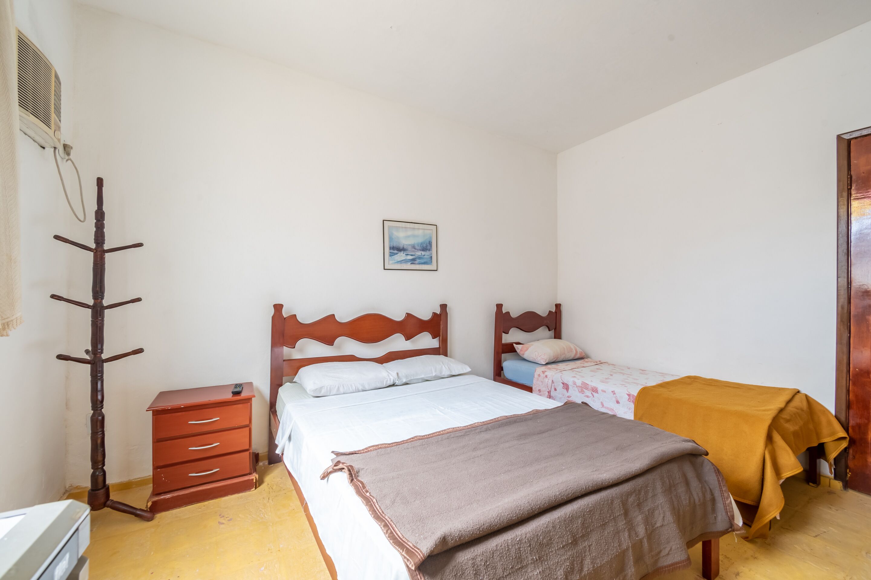 Ein Schlafzimmer mit zwei Betten, einem Holzschrank, einem Kleiderständer und einem Bild an der Wand.