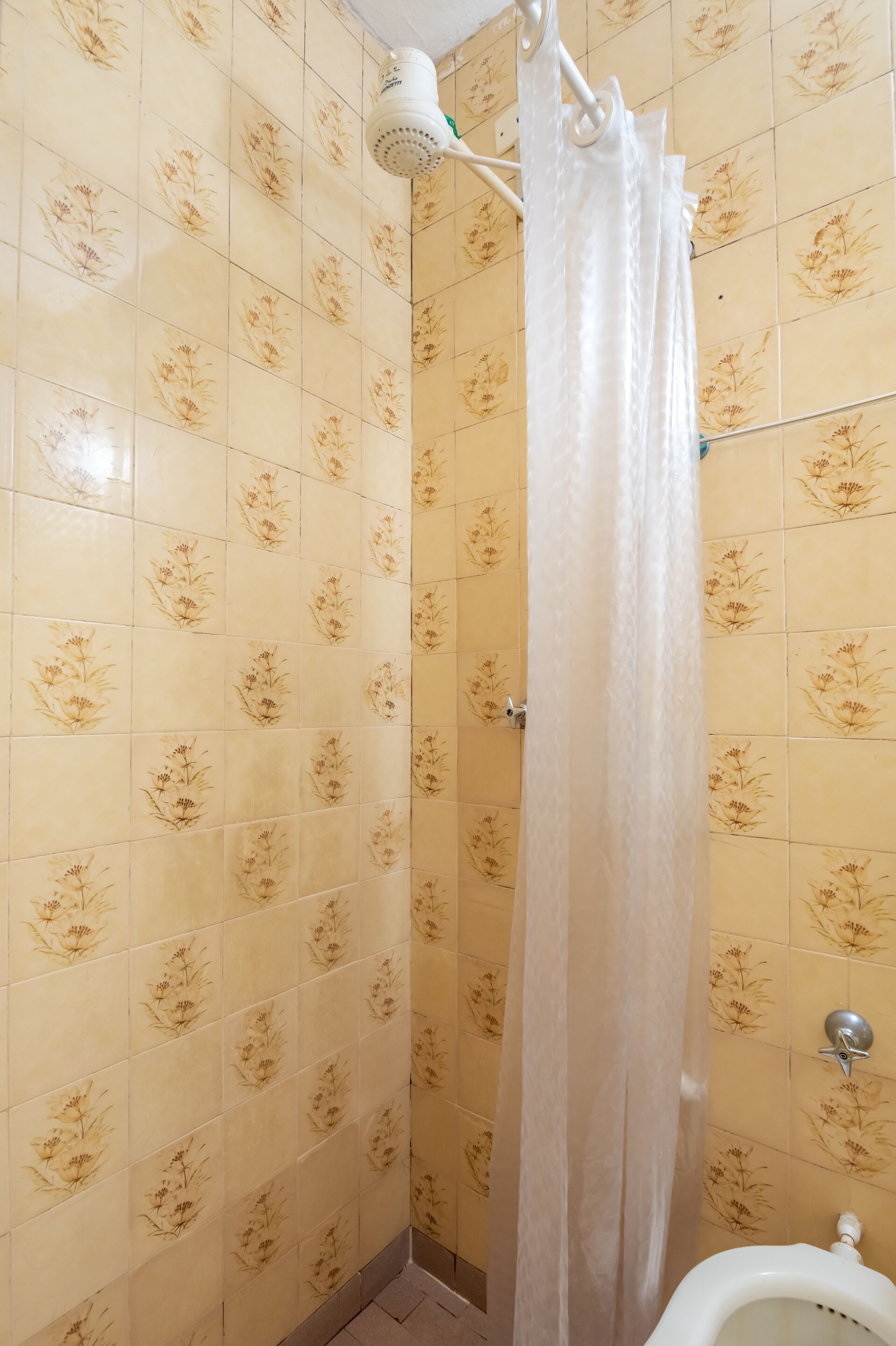 A bathroom with floral patterned tiles, a shower curtain, and a urinal.