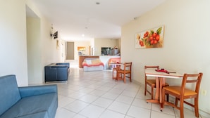 A living room with a blue sofa, a dining table with chairs, and a kitchen in the background. - OYO Residencial Muriqui Apart Hotel, Mangaratiba (Mangaratiba)