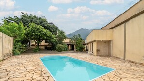 A swimming pool with stone flooring, surrounded by buildings and trees, with mountains in the background. - OYO Residencial Muriqui Apart Hotel, Mangaratiba (Mangaratiba)