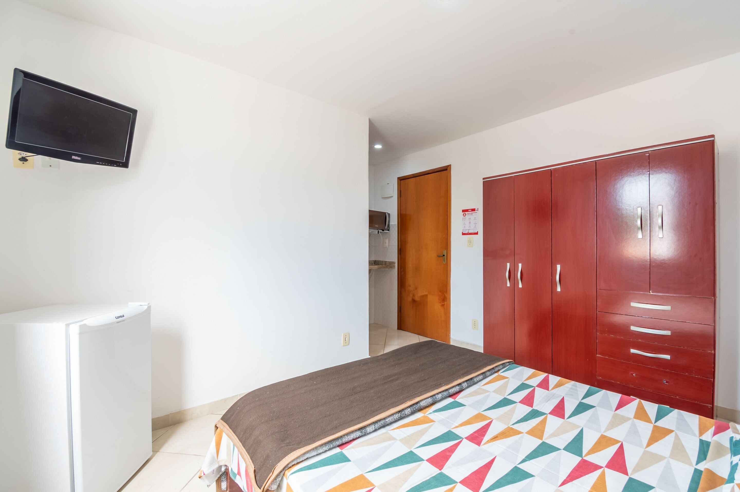 Un dormitorio con cama, televisor, refrigerador y armario.