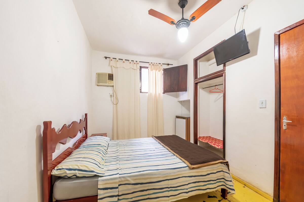 A bedroom with a bed, a ceiling fan, a TV mounted on the wall, and a wardrobe.