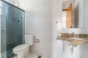 Un baño con ducha de vidrio, inodoro y lavabo con espejo superior.