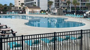 Une piscine dotée de chaises longues et d’un petit pavillon, le tout entouré d’une clôture.