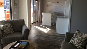 Un salon moderne avec un canapé gris, une table basse sur laquelle sont posés des livres et une petite table en bois. Une porte-fenêtre coulissante donne accès à un balcon.