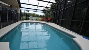 Piscina interior com cobertura de vidro, rodeada por espreguiçadeiras e vista para o exterior.