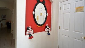 Um corredor com parede vermelha, porta branca e espelho decorado com motivos do Mickey Mouse.