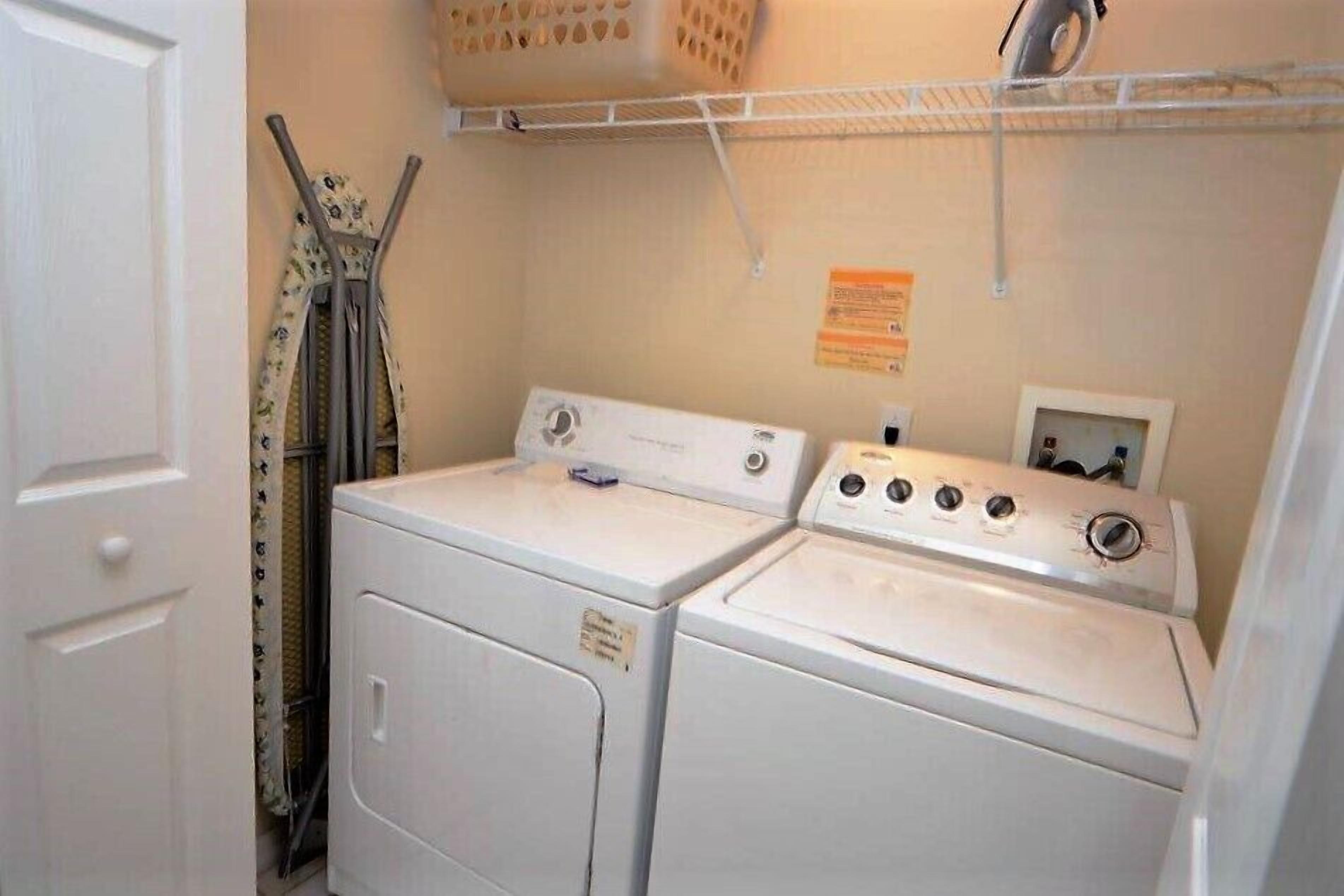A laundry room with two stacked washers and dryers, a drying rack, and a basket on the wall.