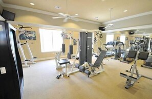 A gym with various exercise equipment, a ceiling fan, and a large window providing natural light.