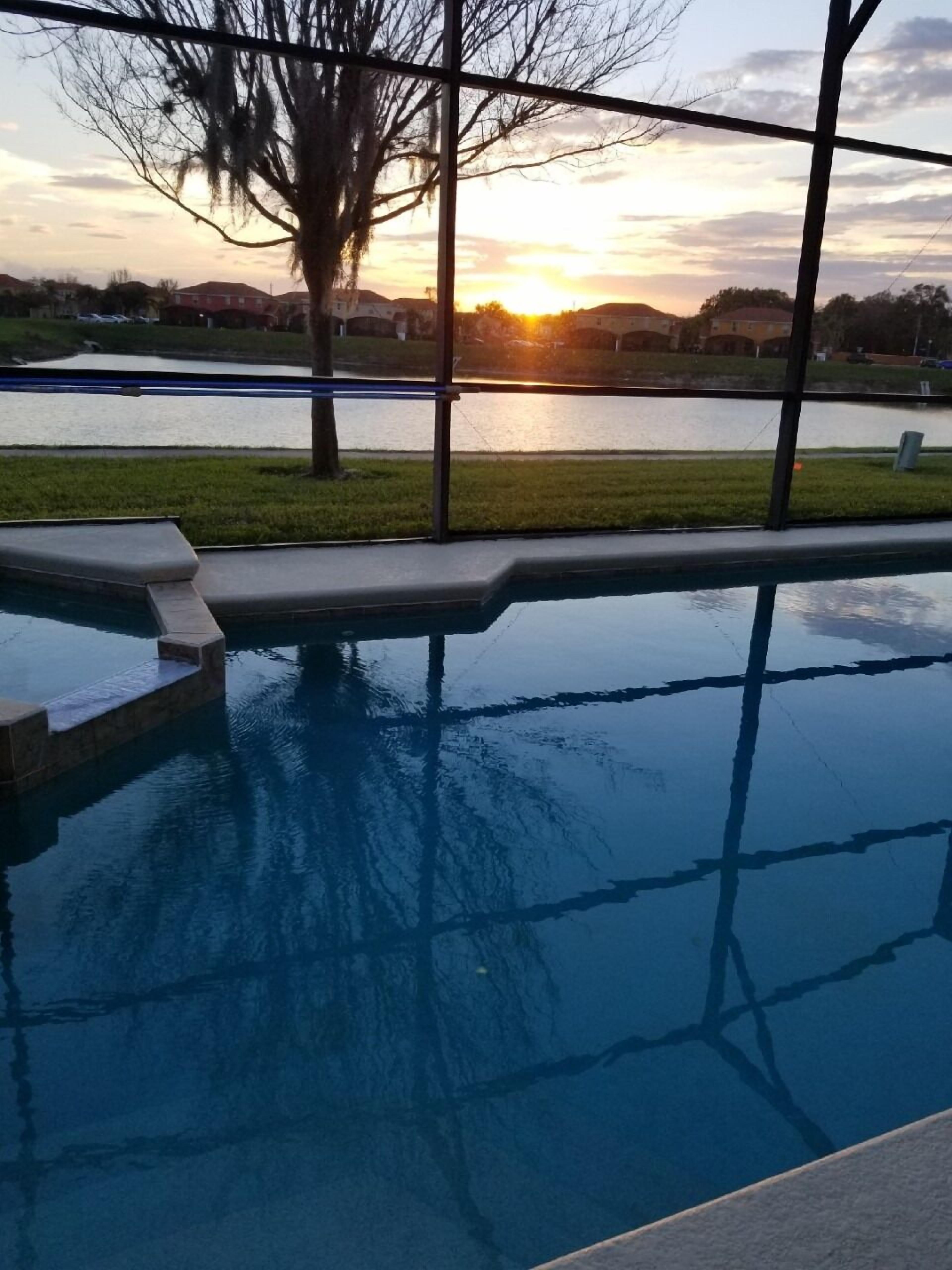 A swimming pool with a view of a sunset over a body of water and a grassy area.
