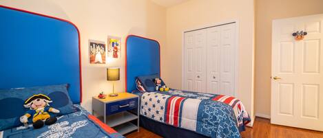 A bedroom with two beds, a nightstand, a lamp, and a closet.