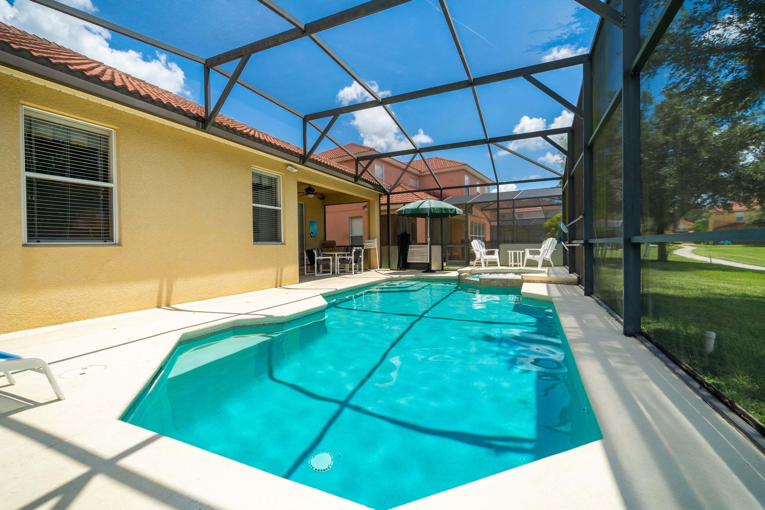 Una piscina interior con agua cristalina y azul, rodeada por un recinto de vidrio, junto a un edificio con fachada amarilla.