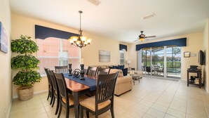 A spacious living area with a dining table, chairs, a sofa, and a large window offering a view of the outdoors. - Bella Vida Resort Luxury Pool Home Game Room View! (Kissimmee)