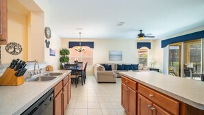 A modern kitchen with wooden cabinets, a dishwasher, and a dining area with a table and chairs. - Bella Vida Resort Luxury Pool Home Game Room View! (Kissimmee)