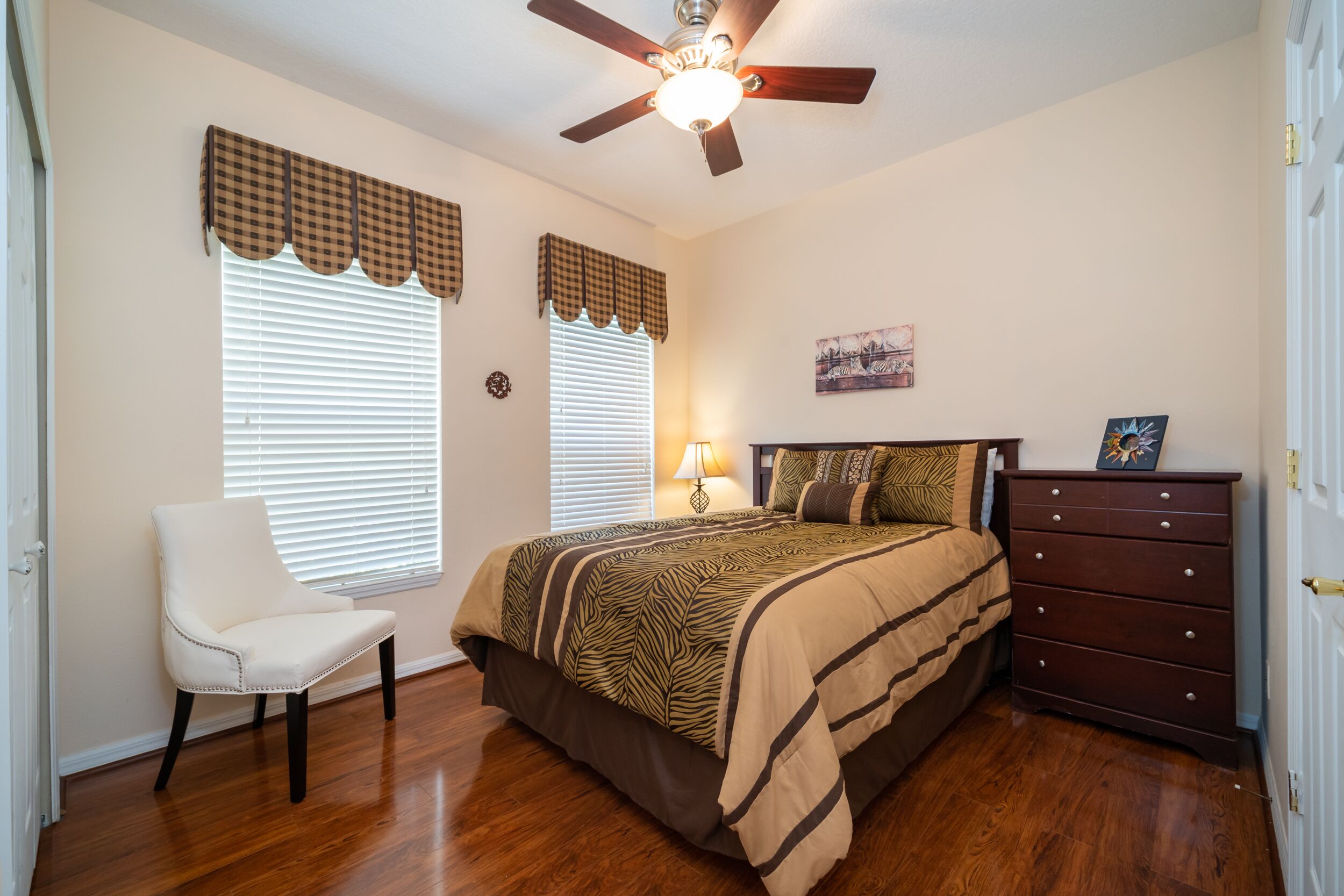 Une chambre à coucher comprenant un lit, une chaise, une commode et un ventilateur de plafond.