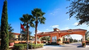 A gated entrance with a red flag, palm trees, and a clear blue sky. - Bella Vida Resort Luxury Pool Home Game Room View! (Kissimmee)