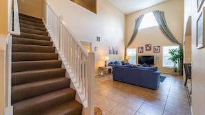 A spacious living area with a staircase, a blue sofa, and a flat-screen TV.