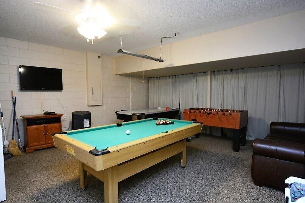 Ein Billardtisch, ein Kicker und ein Fernseher in einem Raum mit Deckenventilator und Vorhängen.