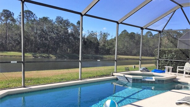 A swimming pool with a view of a lake and trees, surrounded by a covered area with lounge chairs. - 4636 5-bed Disney Area Pool Home, Cumbrian Lakes (Kissimmee)