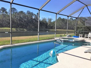 A swimming pool with a view of a lake and trees, surrounded by a covered area with lounge chairs.