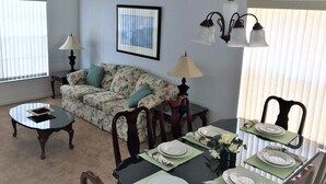 A dining area with a table set for four, a floral sofa, and two lamps. - 4636 5-bed Disney Area Pool Home, Cumbrian Lakes (Kissimmee)
