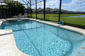 A swimming pool with clear water, surrounded by a fence, and overlooking a green landscape with houses in the background.