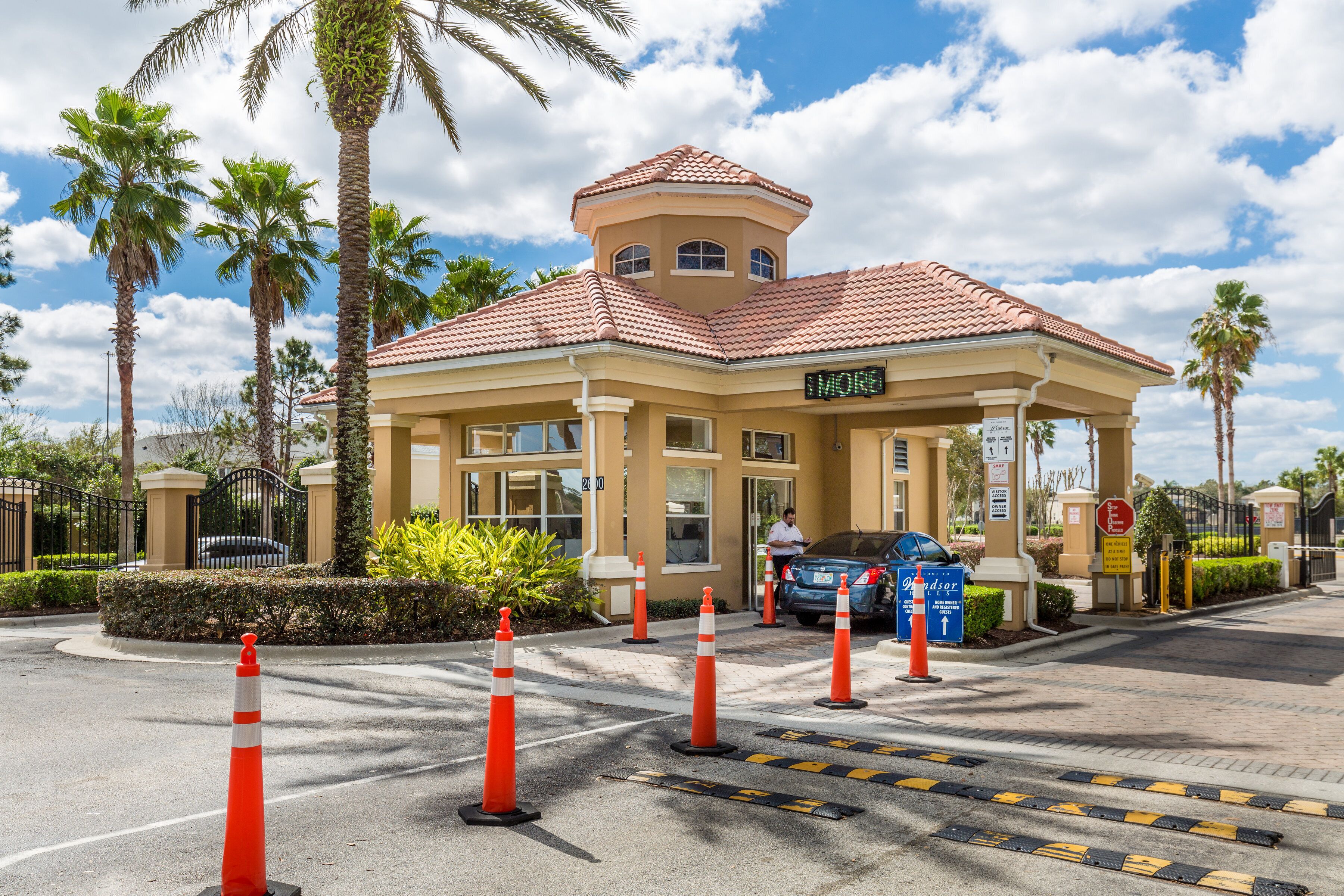 A hotel entrance with a red-tiled roof, palm trees, and orange traffic cones.