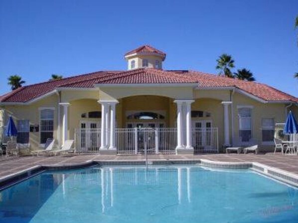 A poolside view of a hotel with a pool, outdoor seating, and a building with a red-tiled roof. - Huge 6-bed Emerald Is Resort- Elite Vacation Homes (Kissimmee)