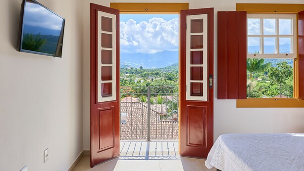 Une chambre dotée d’un lit, d’une télévision et d’un balcon offrant une vue sur un paysage montagneux.