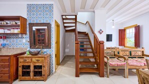 Une cuisine spacieuse avec des meubles en bois, un évier encastré et un crédence carrelée. Un escalier en bois mène à une chambre dotée d’un lit et d’une fenêtre.