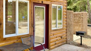 A log cabin with a wooden exterior, a red door, and a patio area with a grill.