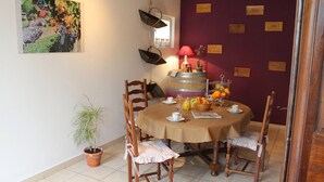 Un espace repas comprenant une table ronde, des chaises, une plante en pot, un tonneau à vin et un mur orné de plaques nominatives.