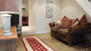 A living room with a brown leather sofa, a red and white rug, a television on a wooden stand, and a wall-mounted artwork.