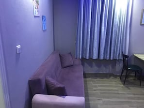 A purple sofa with pillows, a wooden floor, a chair, and a window with curtains.