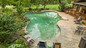 A swimming pool with a stone deck, surrounded by lush greenery and a view of a golf course.