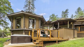 A wooden deck with a hot tub, a covered patio, and a large window overlooking a grassy area.