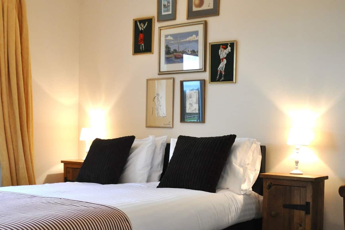 A neatly made bed with a striped blanket, two bedside tables with lamps, and several framed pictures on the wall.
