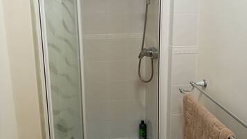 Cabina de ducha con paredes de vidrio, un cabezal de ducha manual y un accesorio de ducha manual.