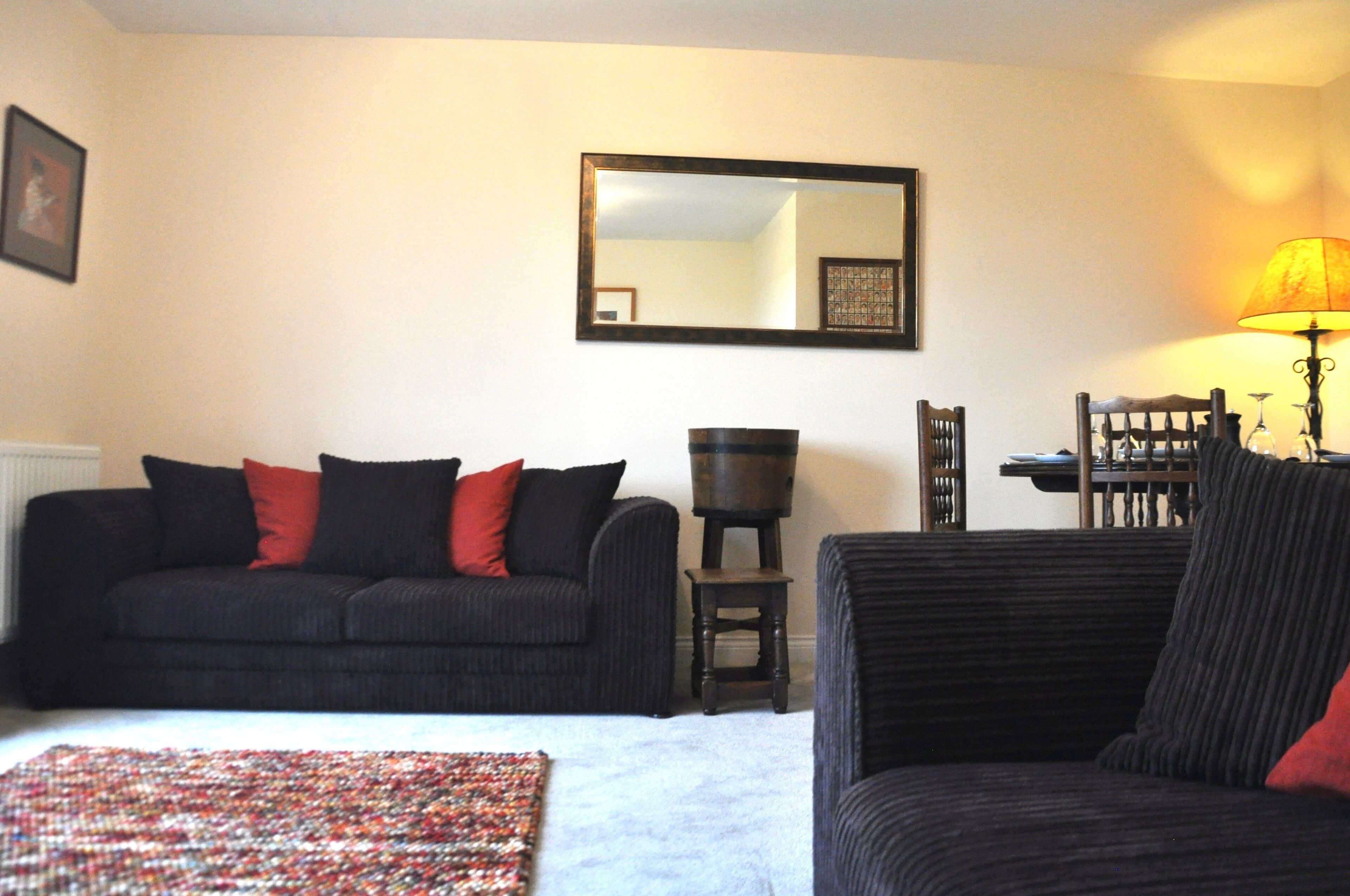 A room with a black sofa, a small table, a lamp, and a mirror on the wall.