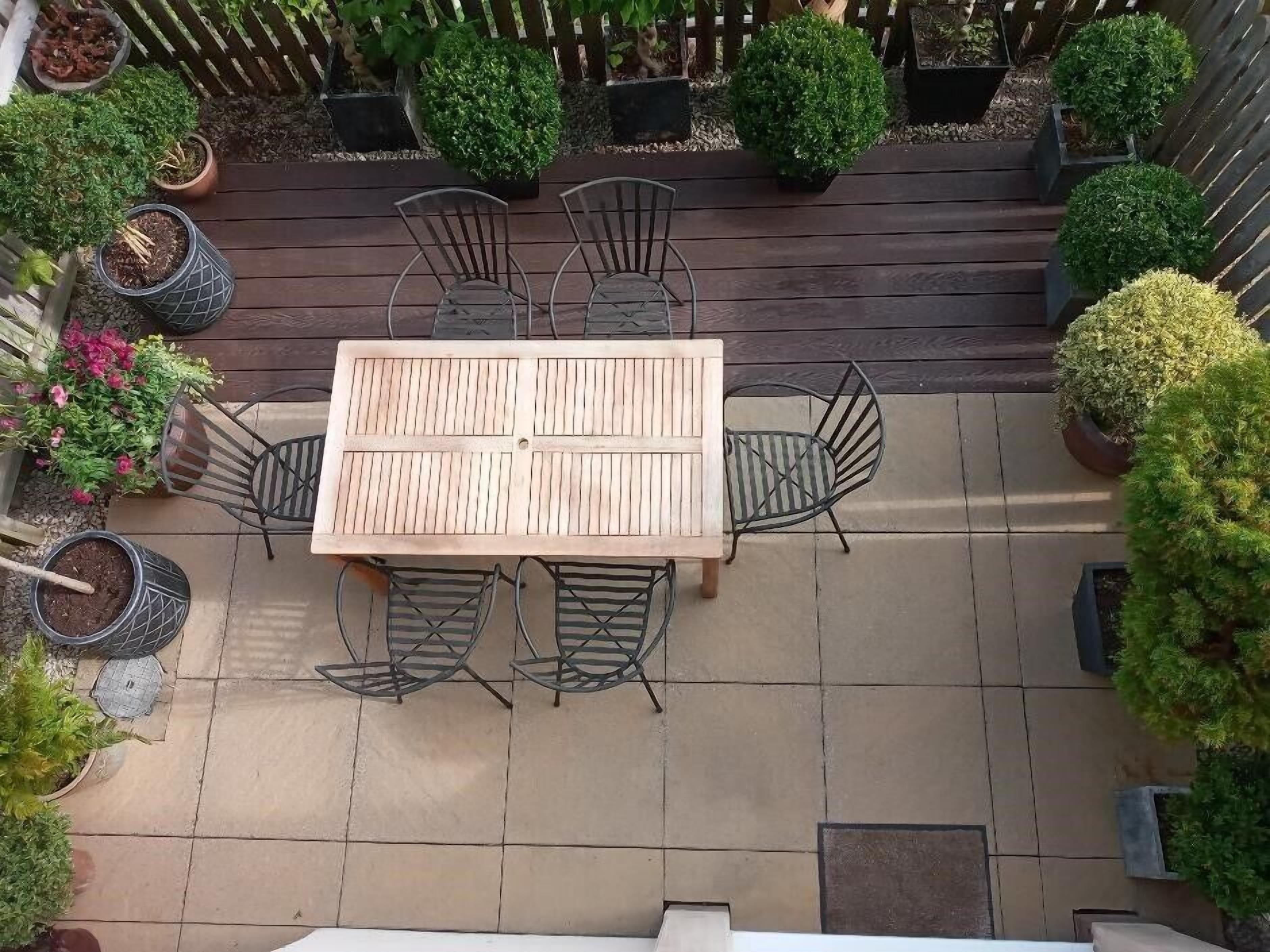 Ein Holztisch mit Metallstühlen, umgeben von Topfpflanzen und einer Holzterrasse.