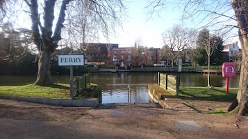 A sign reading "FERRY" near a body of water with a bridge, trees, and buildings in the background.
