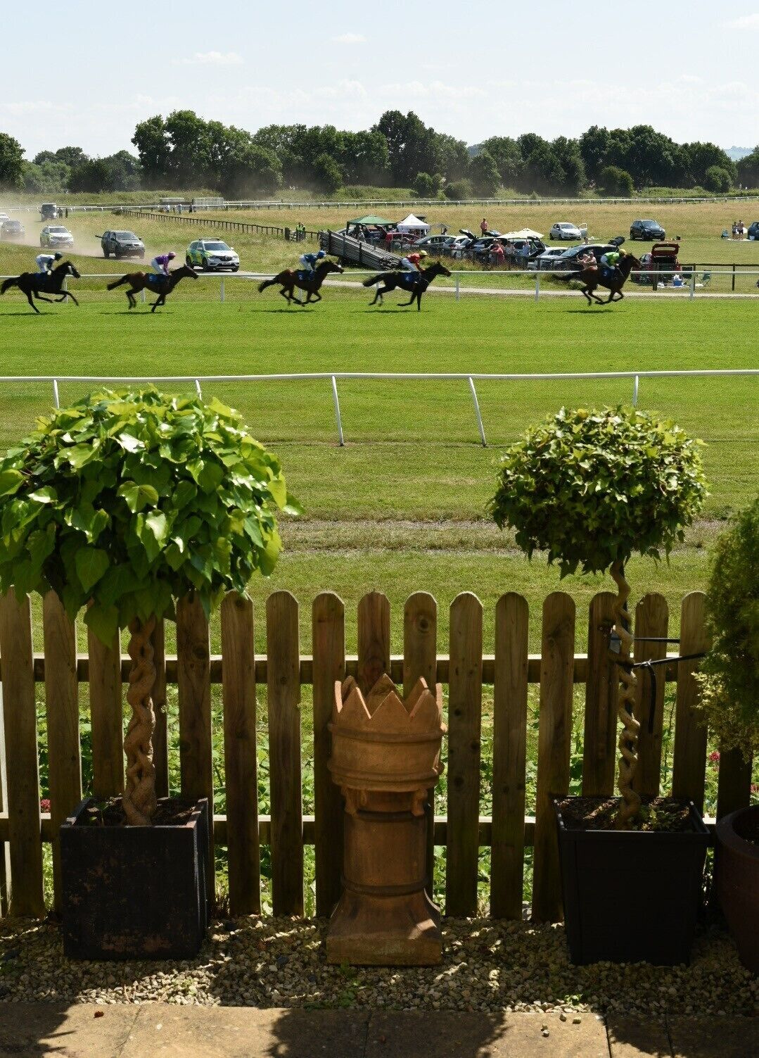 A horse race track with a wooden fence, potted plants, and a clear sky.